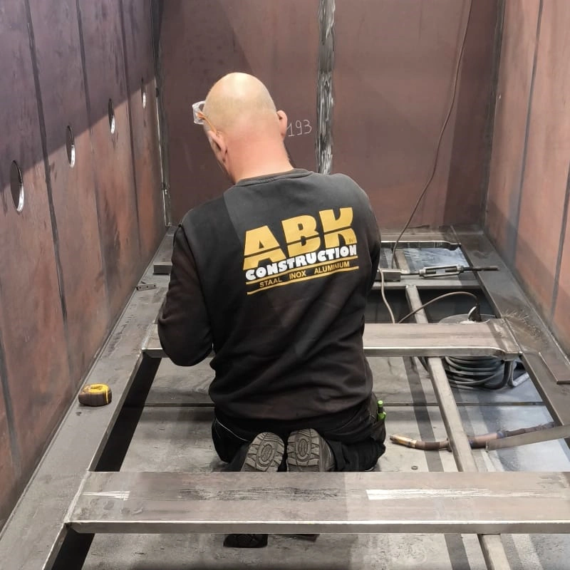 ABK Construction-lasser knielt en werkt aan stalen frame binnen grote metalen constructie.